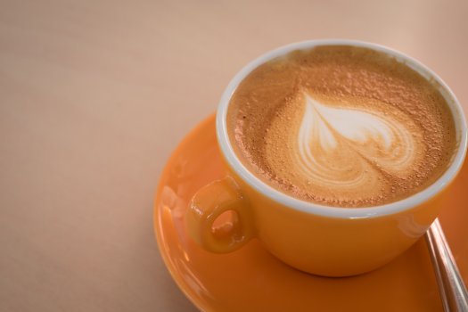 A flat-white served in a bright orange cup and saucer.