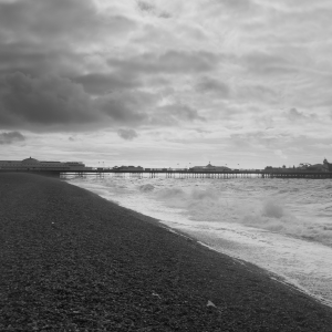 Brighton Pier seen from a few hundred meters away, showing it going from the road into the sea. Over Bright are some stormy looking clouds.