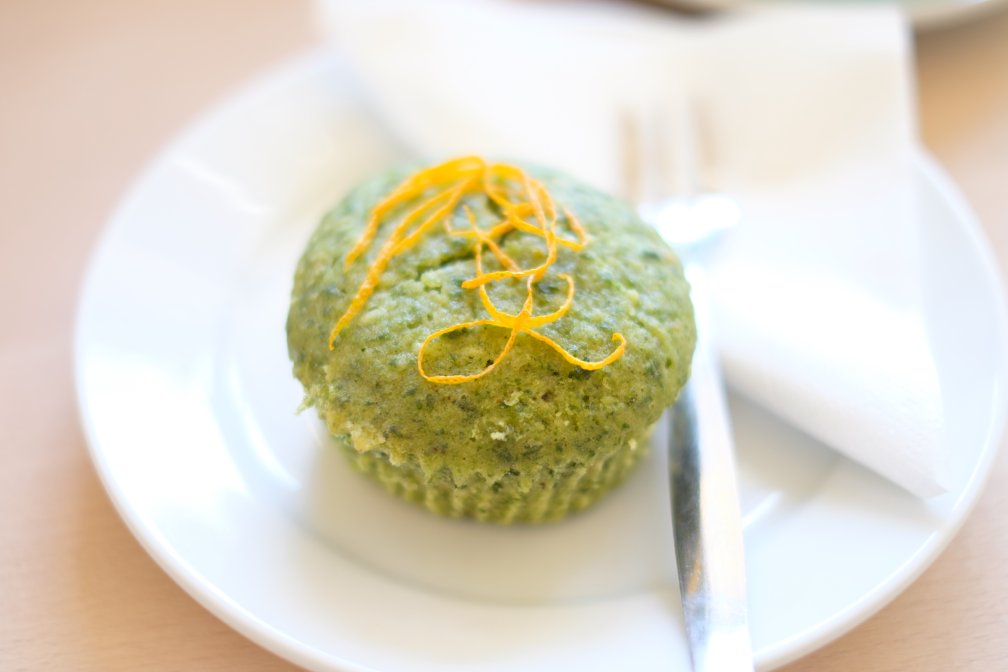 A softly lit photo of a cupcake made with green sponge with a trail of fine orange peel on top.