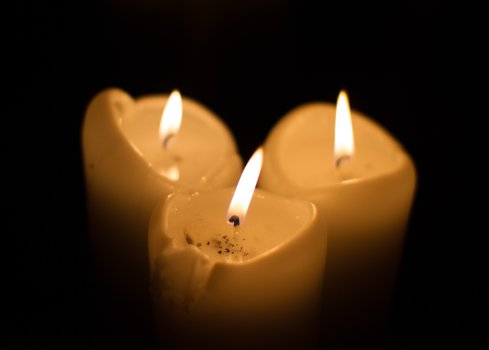 A cluster of three large candles glowing in the dark.