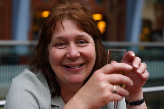 A head and shoulders shot of my Mum relaxing with a glass of something in her hands, with a blurry St Pancras station behind her.