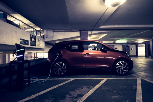 An orange BMW i3 in a moodily lit car park plugged into a charge point.