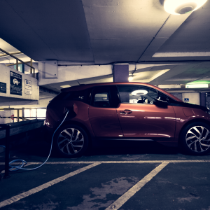 An orange BMW i3 in a moodily lit car park plugged into a charge point.