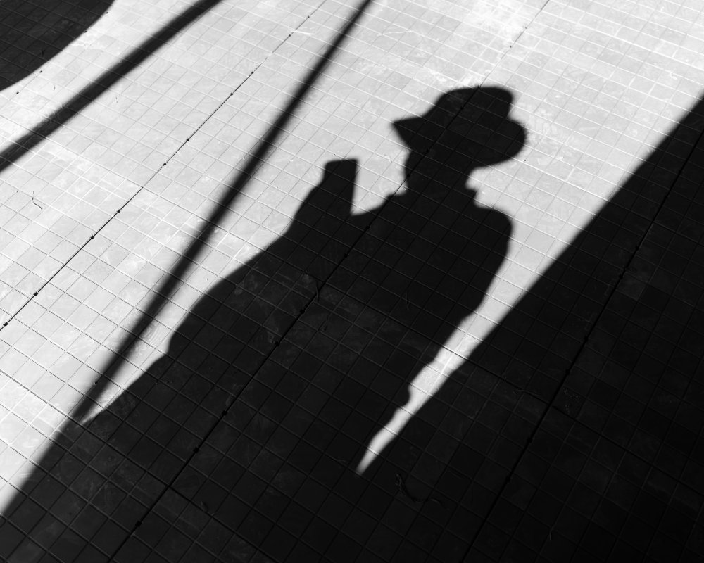 A photo of the ground showing a shadown of a person in a hat checking their phone.
