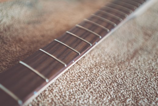 A close up photo of a guitar fretboard, shot with a very low depth of field, so that just one fret is in focus, and the rest of the neck blurs out very quickly.