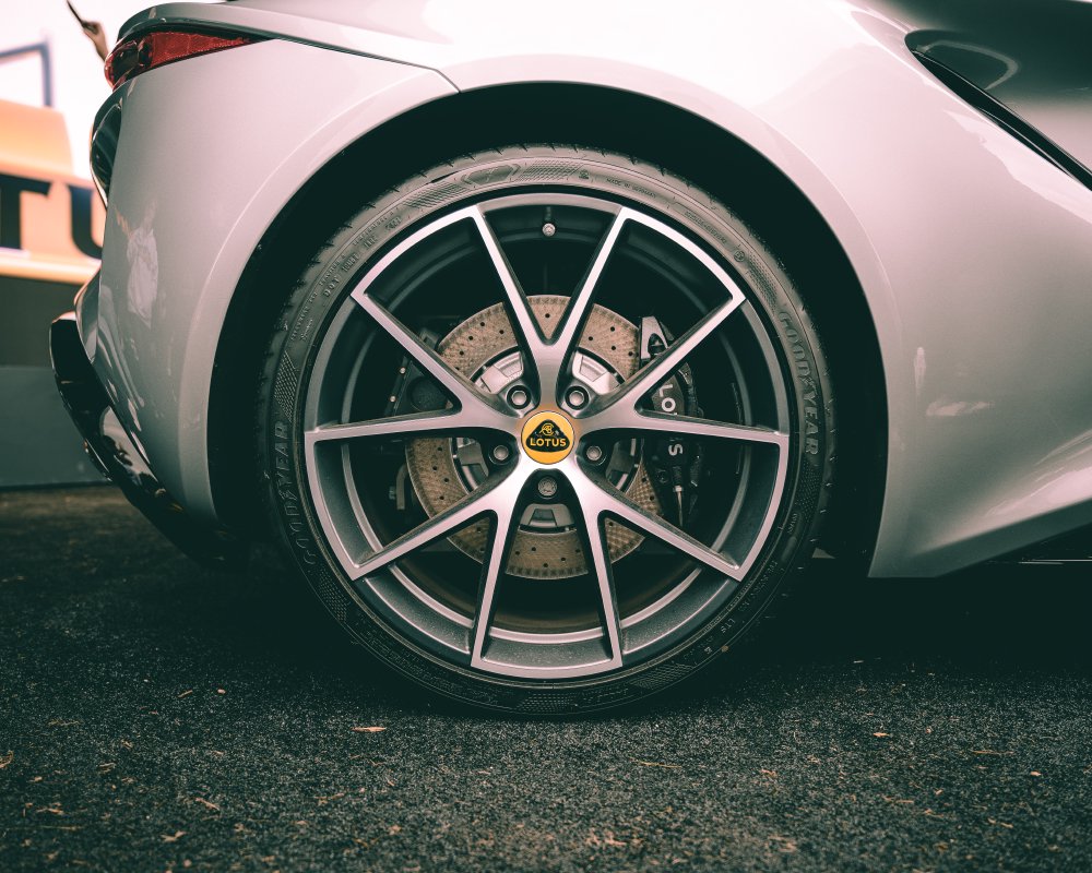 A close-up photo of the rear wheel of a Lotus Emira. The wheel has been aligned perfectly to ensure the Lotus logo is level and the air valve is perfectly at noon on the wheel. The break disk has a nice swirly pattern in the metal.