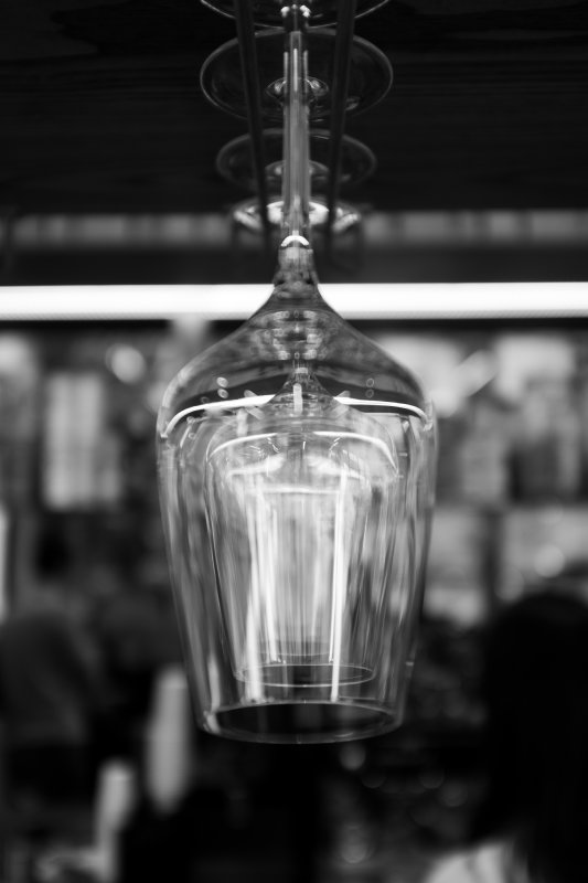 A photo from the end of a line of glasses hung up in a bar, with the further back glasses visible through the front one, with lots of lights reflected in the glass.