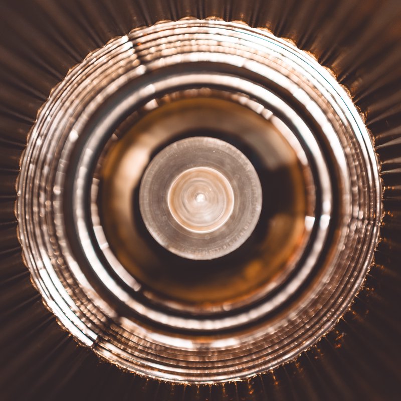 A somewhat abstract photo of the bulb and golden shade of a lamp, emphasising the circles of the shade and the bulb.