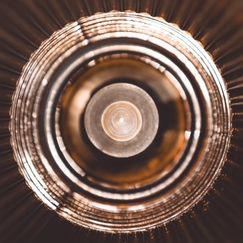 A somewhat abstract photo of the bulb and golden shade of a lamp, emphasising the circles of the shade and the bulb.