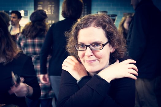 A photo of Laura looking at the Camera with her arms crossed, sat in Fitzbillies cafe.