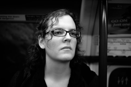 A closeish photo of Laura stood on the London underground, staring into the middle distance.