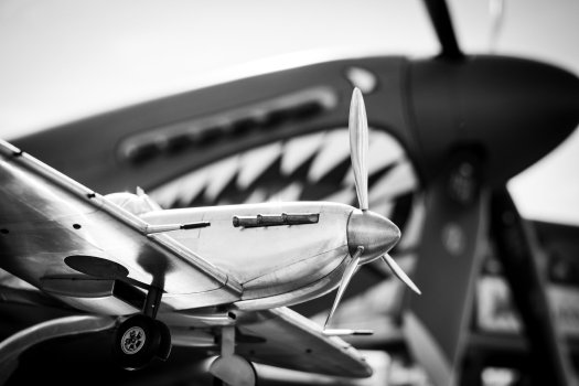 A photo of a chrome model of a spitfire airplane behind which is stood the real thing.