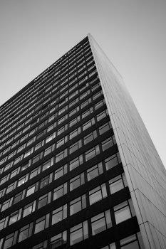 A photo looking up a tall office block that has very uniform windows in black wall on one side and white wall panels on the other. At the top you can just make out a sign reading "Manchester One"