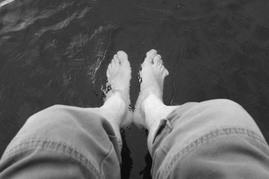 A photo taken looking down at my legs and feet, with my feet in the water of a lake, causing ripples.