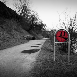 A photo of a park sign that has been graffiti'd to have a face where the smile looks a bit like the pepsi logo.