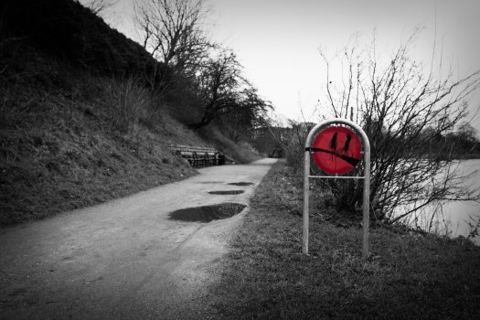 A photo of a park sign that has been graffiti'd to have a face where the smile looks a bit like the pepsi logo.