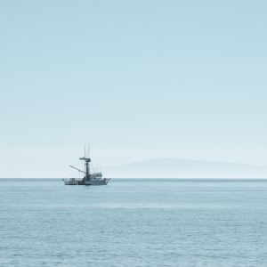 A mid sized personal boat sits on the ocean, with the sky, water, and boat all being a similar light shade of blue.