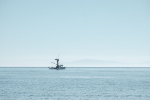 A mid sized personal boat sits on the ocean, with the sky, water, and boat all being a similar light shade of blue.