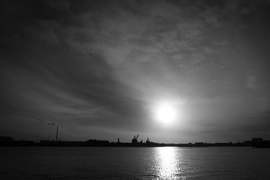 A high contrast shot of the view of a old and new dock buildings and cranes under the setting sun.