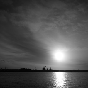 A high contrast shot of the view of a old and new dock buildings and cranes under the setting sun.