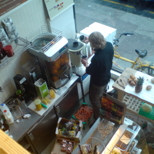 The view from a mezzanine level down onto the bar of a coffee shop where a barista is preparing a drink.