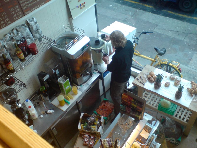 The view from a mezzanine level down onto the bar of a coffee shop where a barista is preparing a drink.