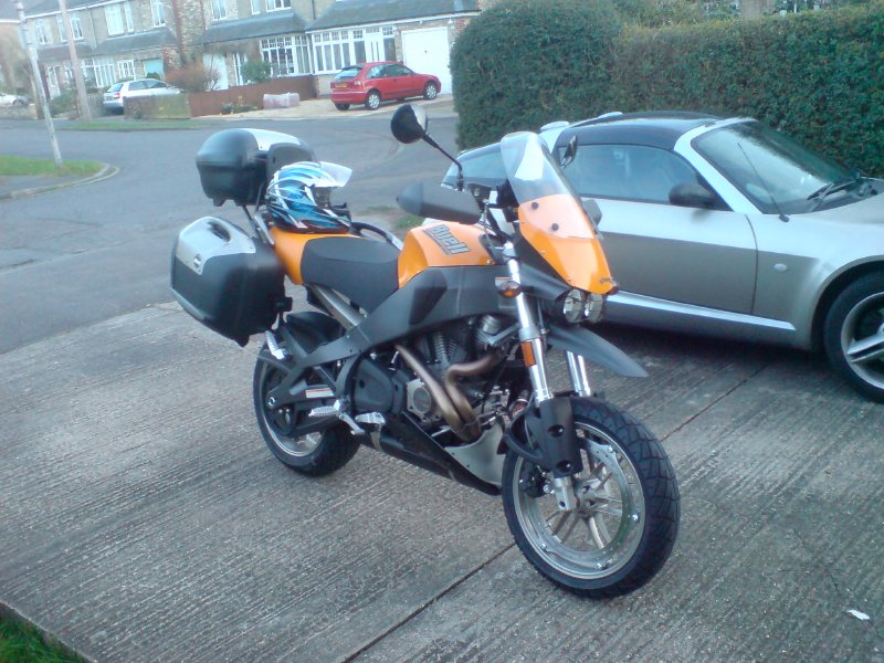 A big yellow and black motorbike sits on the driveway towering over our Smart Roadster.