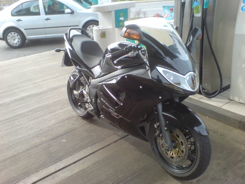 A a big black sportish looking bike parked next to some petrol pumps.