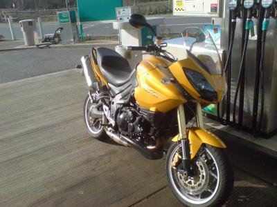A tall yellow motorbike parked next to some petrol pumps.
