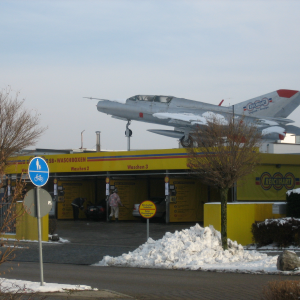 A car wash centre with people cleaning cars that has a vintage MIG fighter jet on the roof.