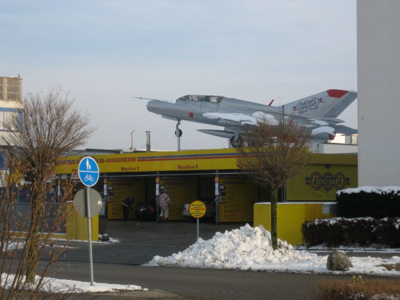 A car wash centre with people cleaning cars that has a vintage MIG fighter jet on the roof.