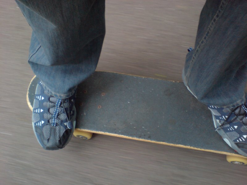 A picture of my feet on a skateboard as it whizzes along some pavement.