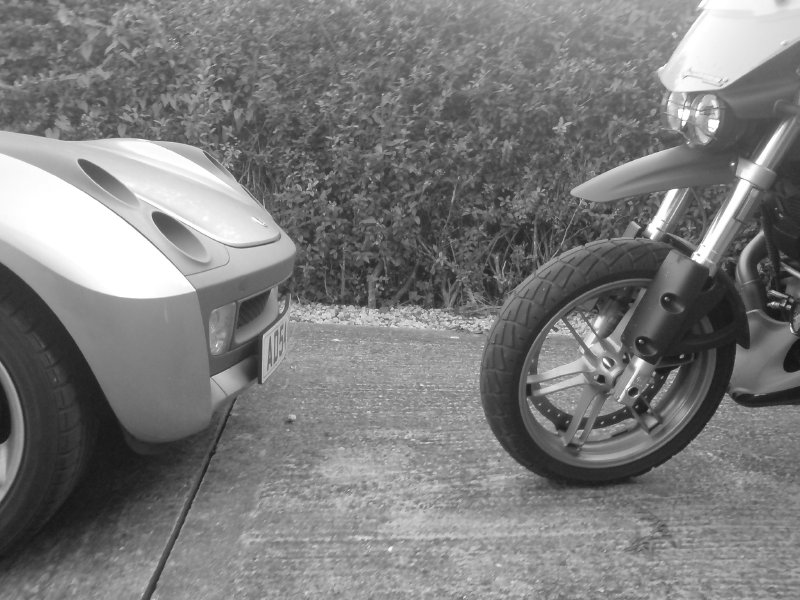 The front bonnet of the smart roadster on the left, the front wheel and beak of the buell ulysses on the right, looking at each other.