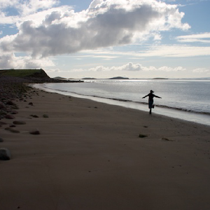 A long empty beach cove, with Laura running down it arms outstretched.
