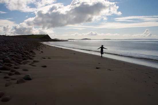 A long empty beach cove, with Laura running down it arms outstretched.