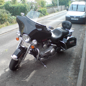 A big black touring Harley Davidson motorbike, parked on a narrow Cambridge street.