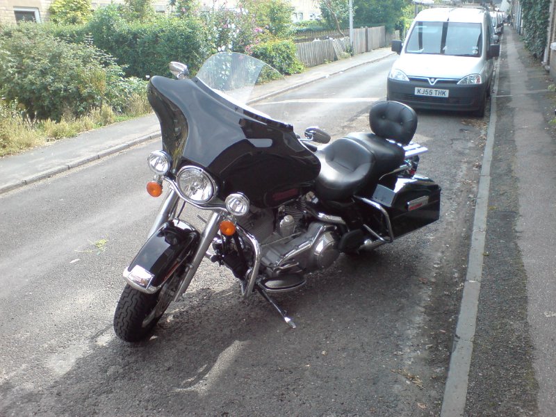 A big black touring Harley Davidson motorbike, parked on a narrow Cambridge street.