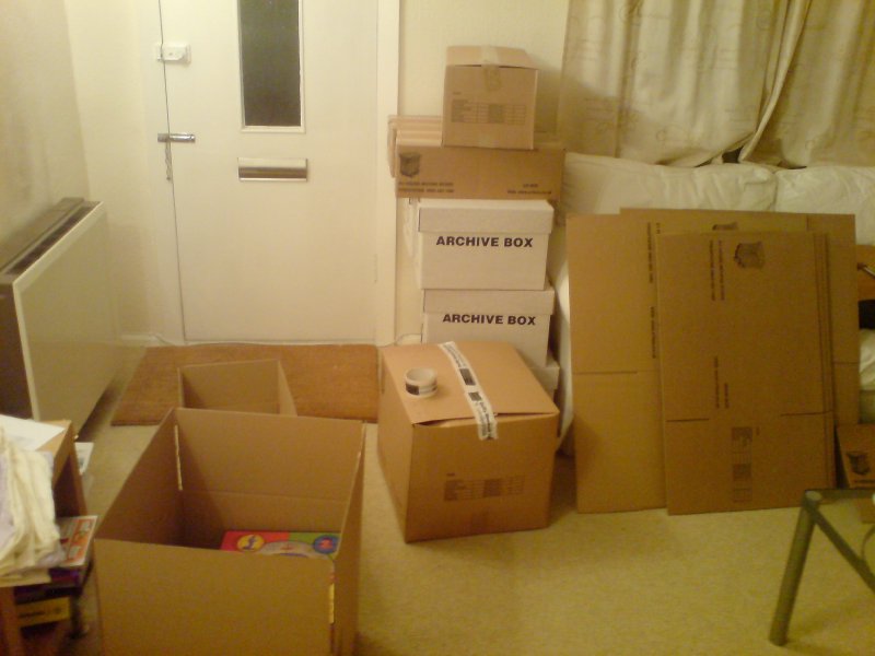 A photo of a front room with everything piled into boxes.