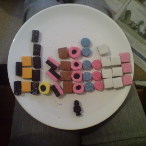 A plate of liquorice all-sorts arranged into a histogram on a plate, with a single liquorice shaped like a person at the bottom of the plate.