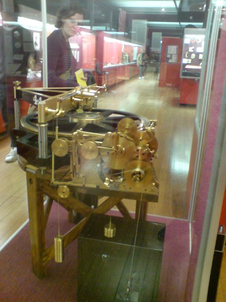 A large gold clockwork machine made of cogs in a class cage.