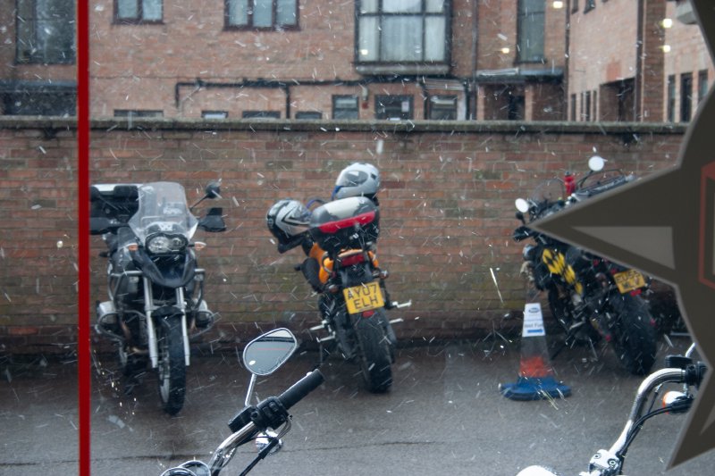 A view out of a window of some motorbikes in the wet, with a small amount of snow falling.