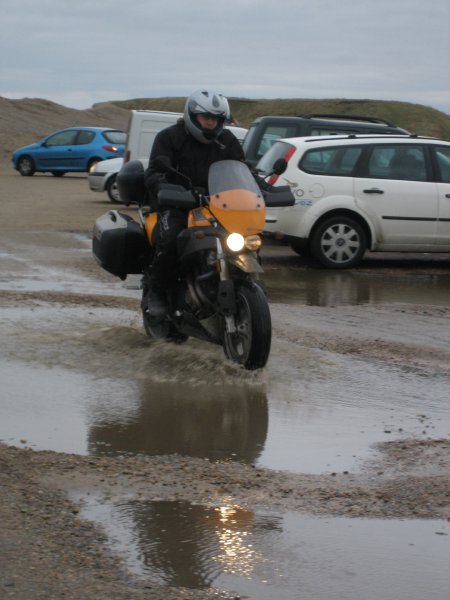 Me driving an orange muddy motorcycle through some deep puddles to get out the car park.