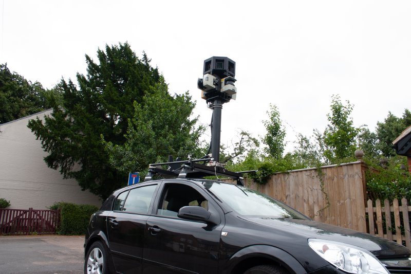 A small hatchback car with a stick on the top upon which is a large camera array.