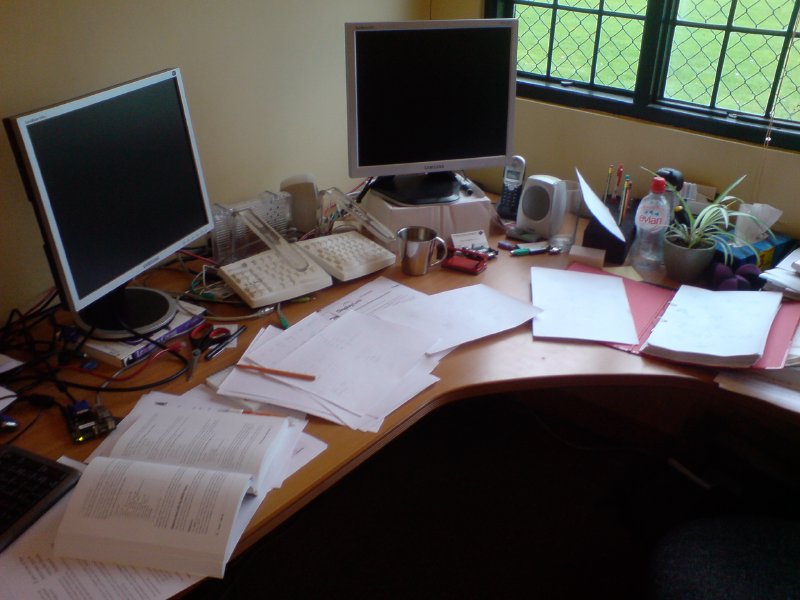 A desk covered in sheets of A4 paper and two monitors, both of which are turned off.