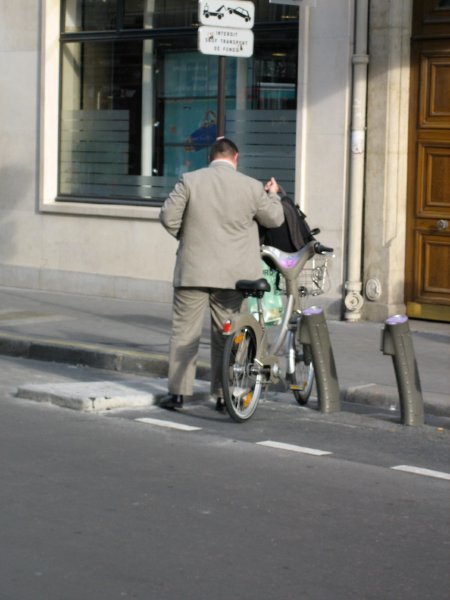 A man either collecting or taking a velib hire pushbike on a Paris street.
