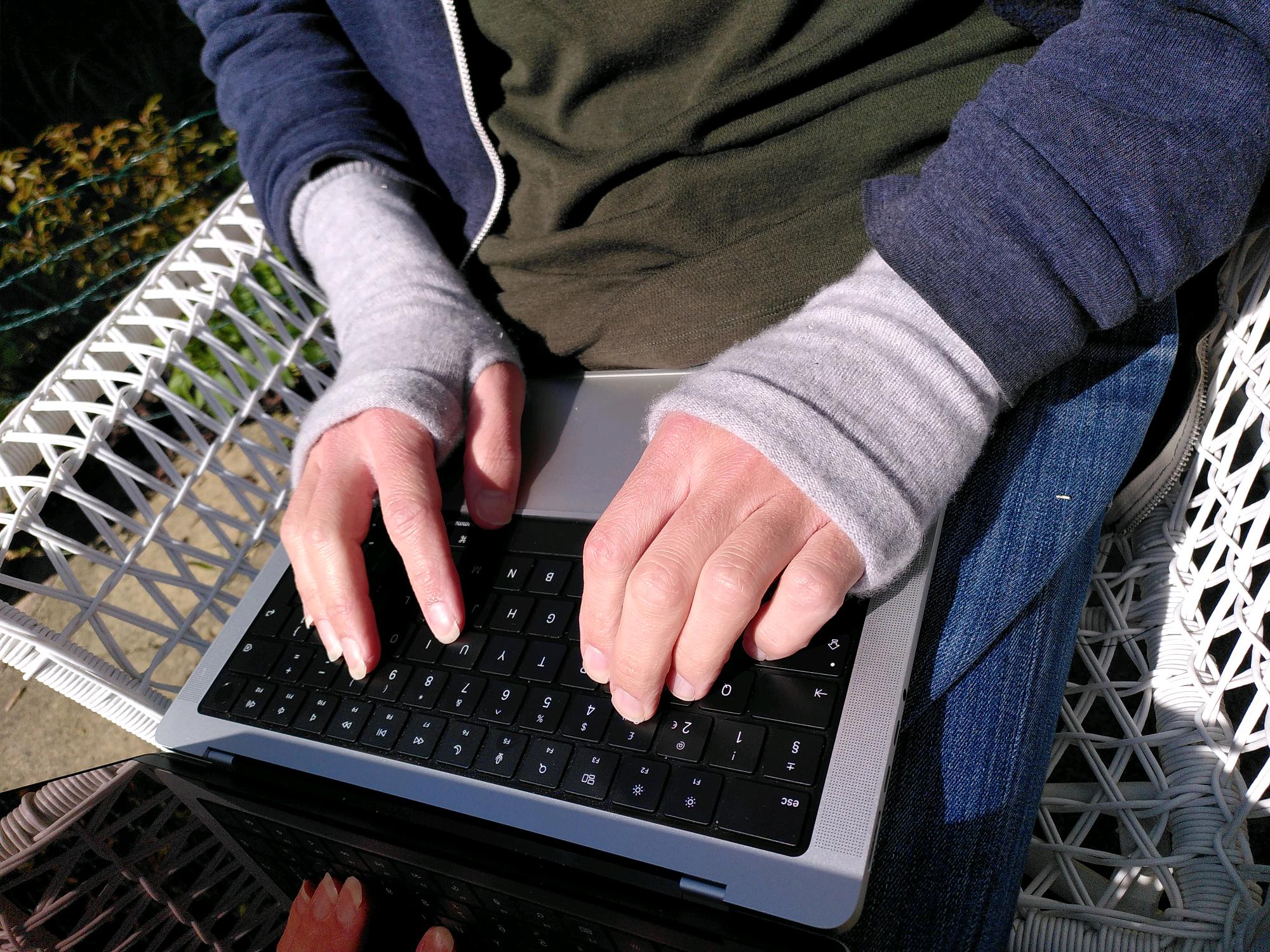 My hands on my laptop keyboard where my wrists and hands are covered in woolen tubes that leave my thumb and fingers free.