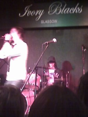 A blurry cellphone shot of a drummer and singer on a stage.
