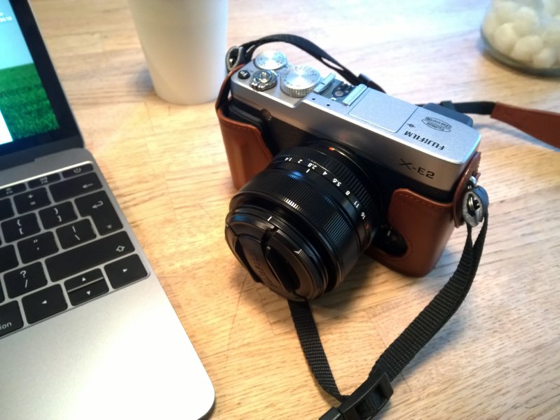 A picture of A Fujifilm X-E2 camera sat next to a laptop and a coffee cup.