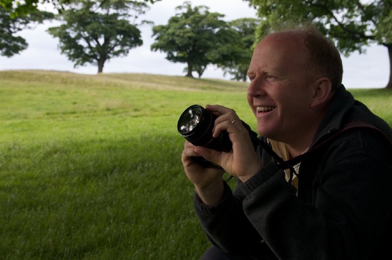 A photo of a person holding a camera looking off into the distance with a big smile on their face.