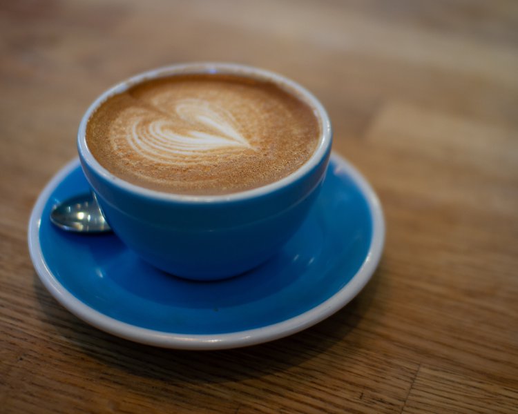 A photo of a flat white in a blue cup with saucer.